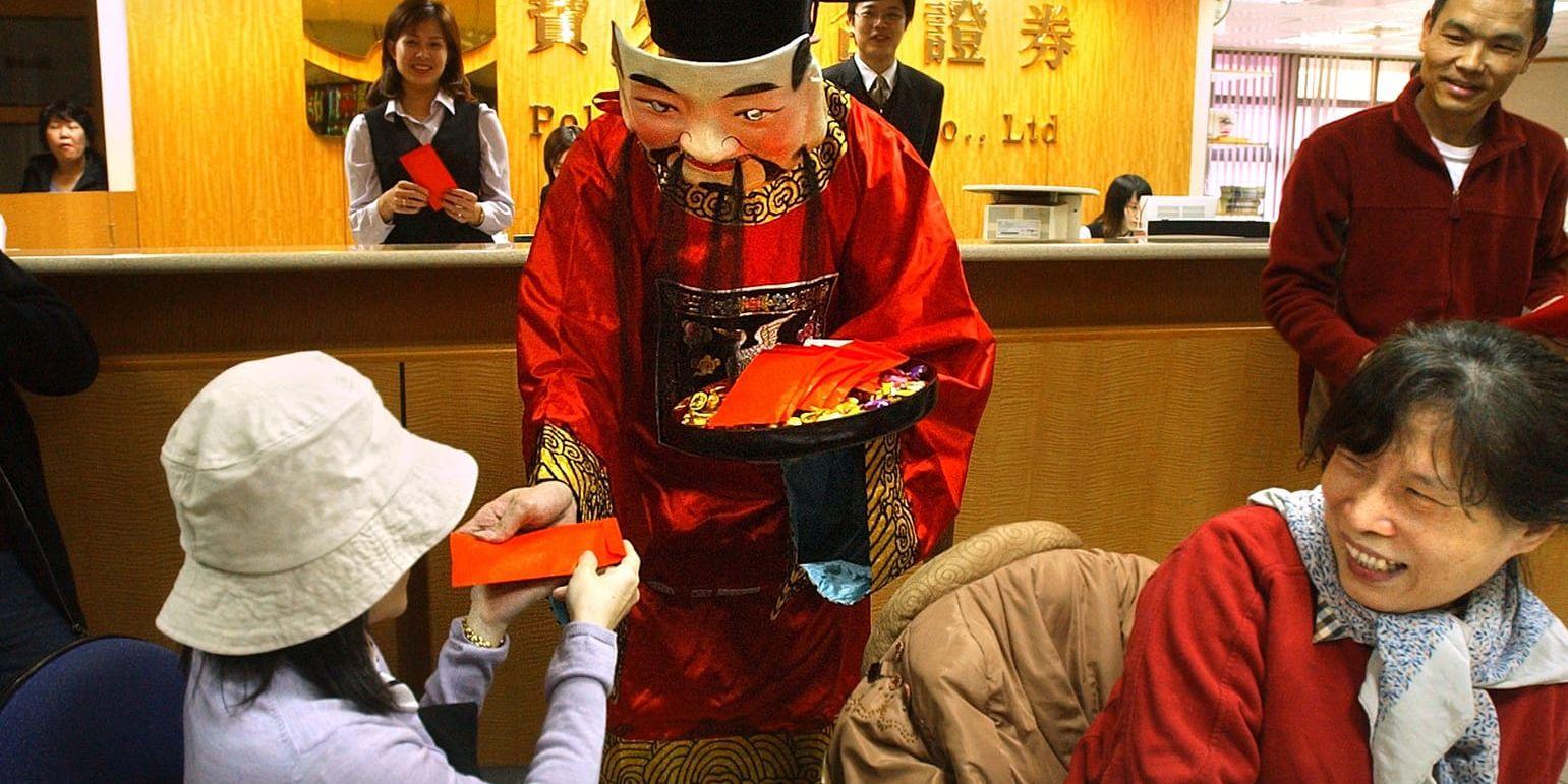En man som är utklädd till en kinesisk gud delar ut röda nyårskuvert. 