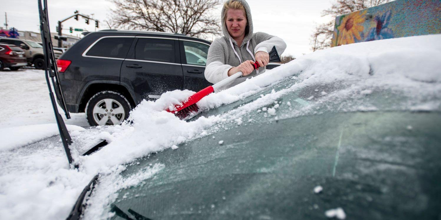 En kvinna skrapar en isig ruta på en snötäckt bil.
