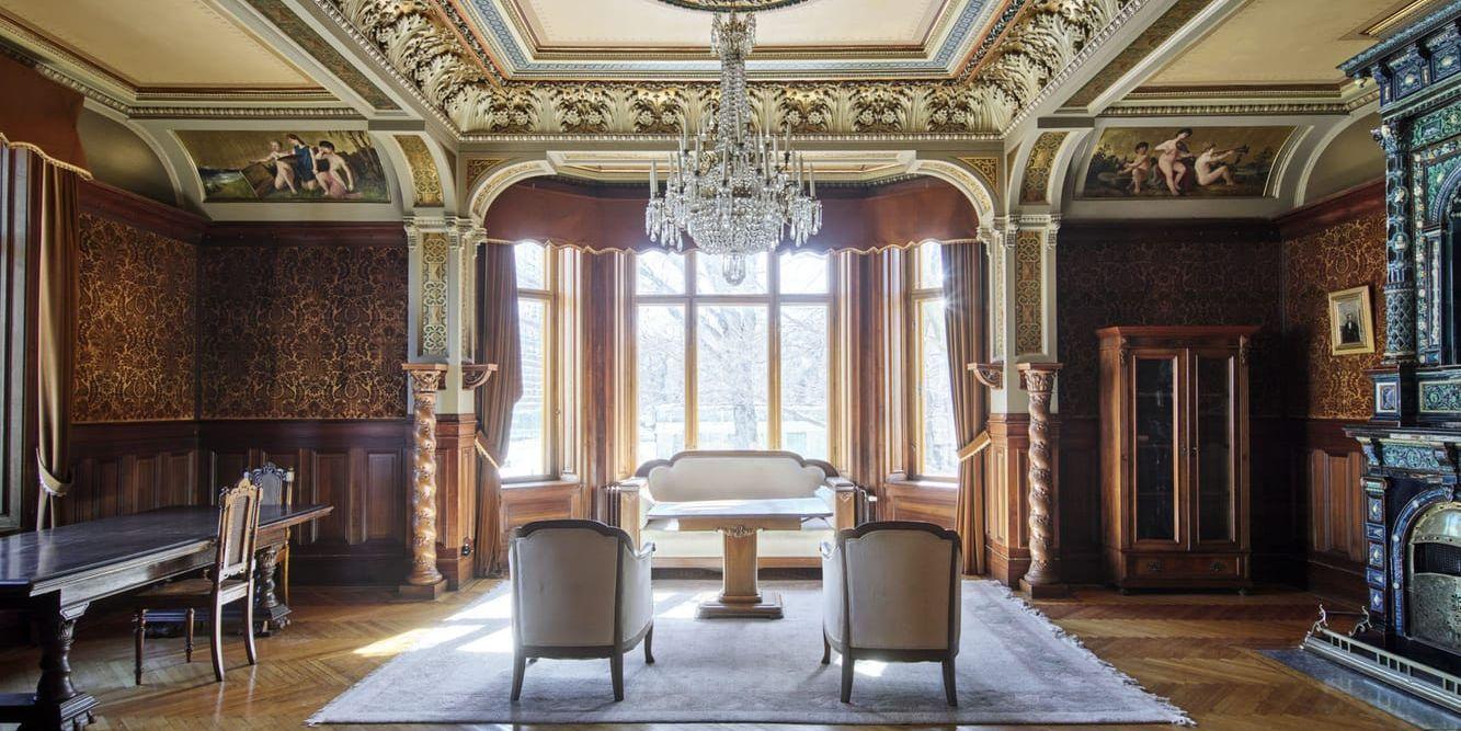 Salong med mörka träpaneler, stuckaturer och en dekorerad kakelugn i Gegerfeltska villan.