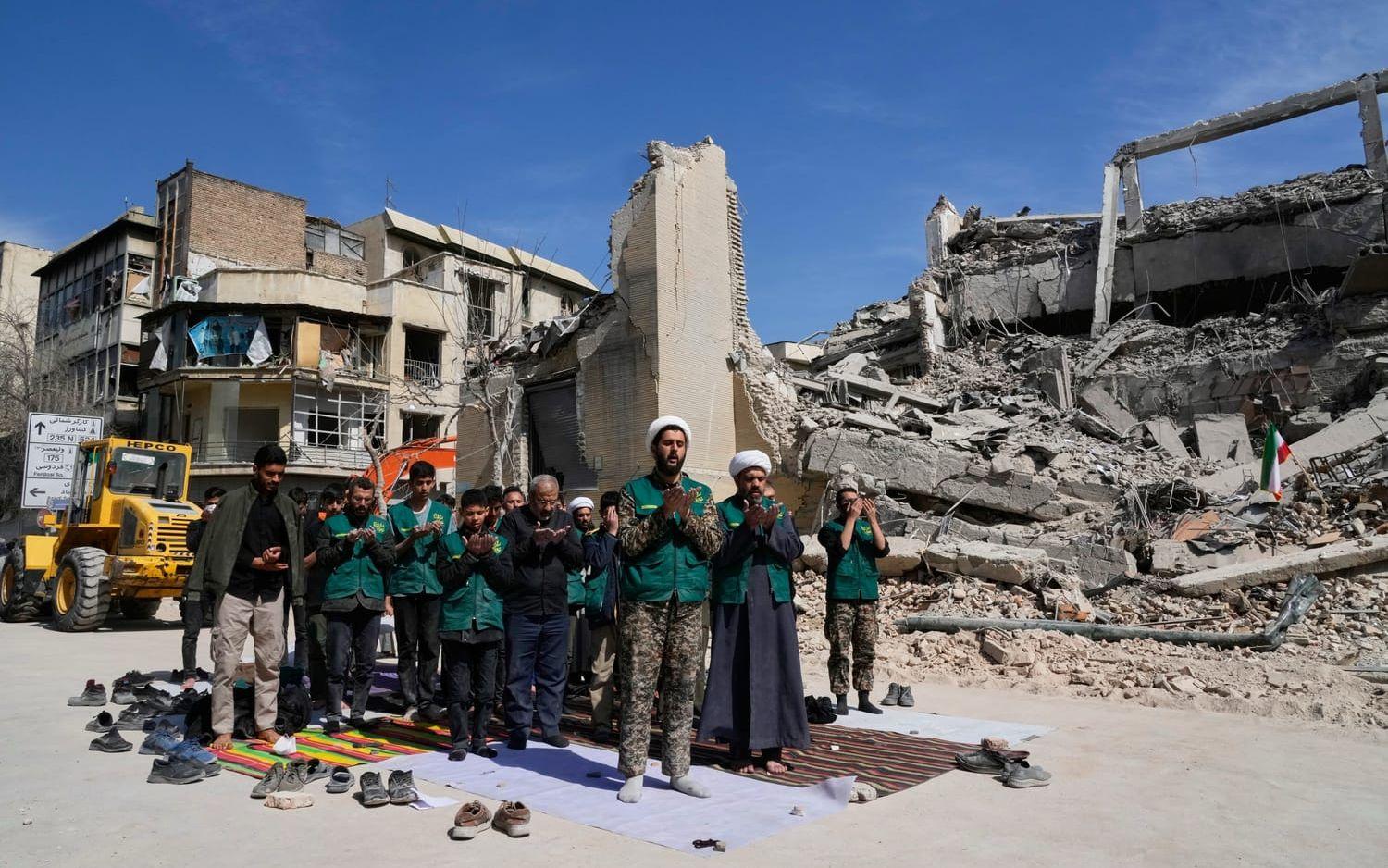 En grupp frivilliga ber vid en byggnad i Teheran som förstörts i Irankriget, som inleddes med Israels och USA:s attacker i helgen.