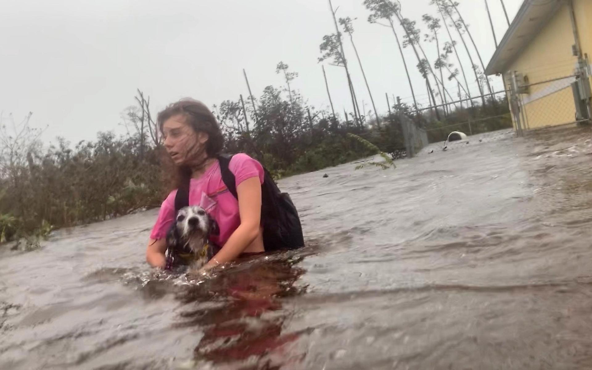 Julia Aylen vadar genom översvämningen med sin hund i famnen i Freeport, Bahamas. 