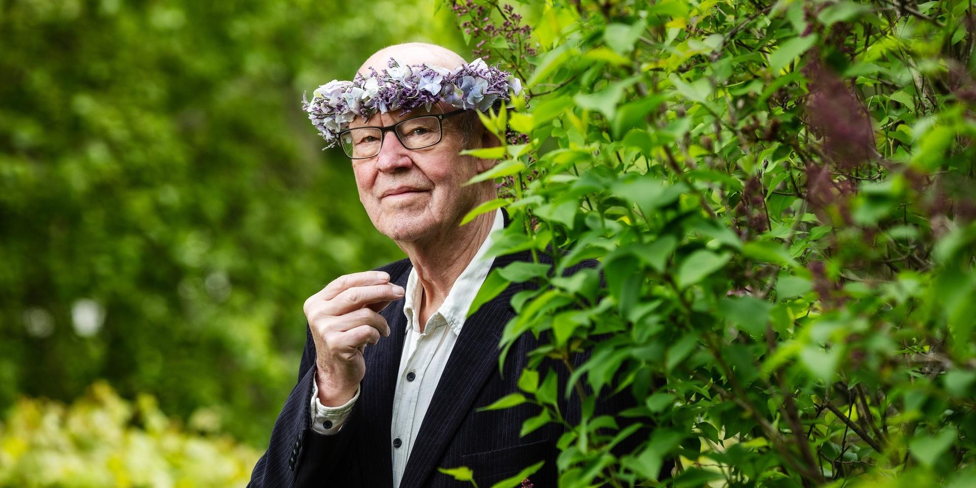 Sten Ljunggren poserar för Sommar i P1. Han har blomsterkrans, glasögon, vit skjorta och mörk kavaj. 
