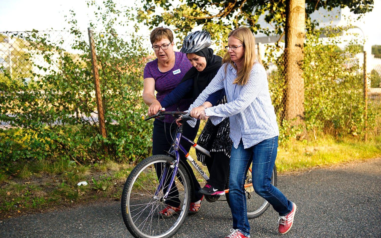 Volontärerna Ingrid Rasmusson (t.v) och Anna Gustavsson Rostamzadeh (t.h) hjälper Fahima Ahmadyar att hålla cykeln upprätt.