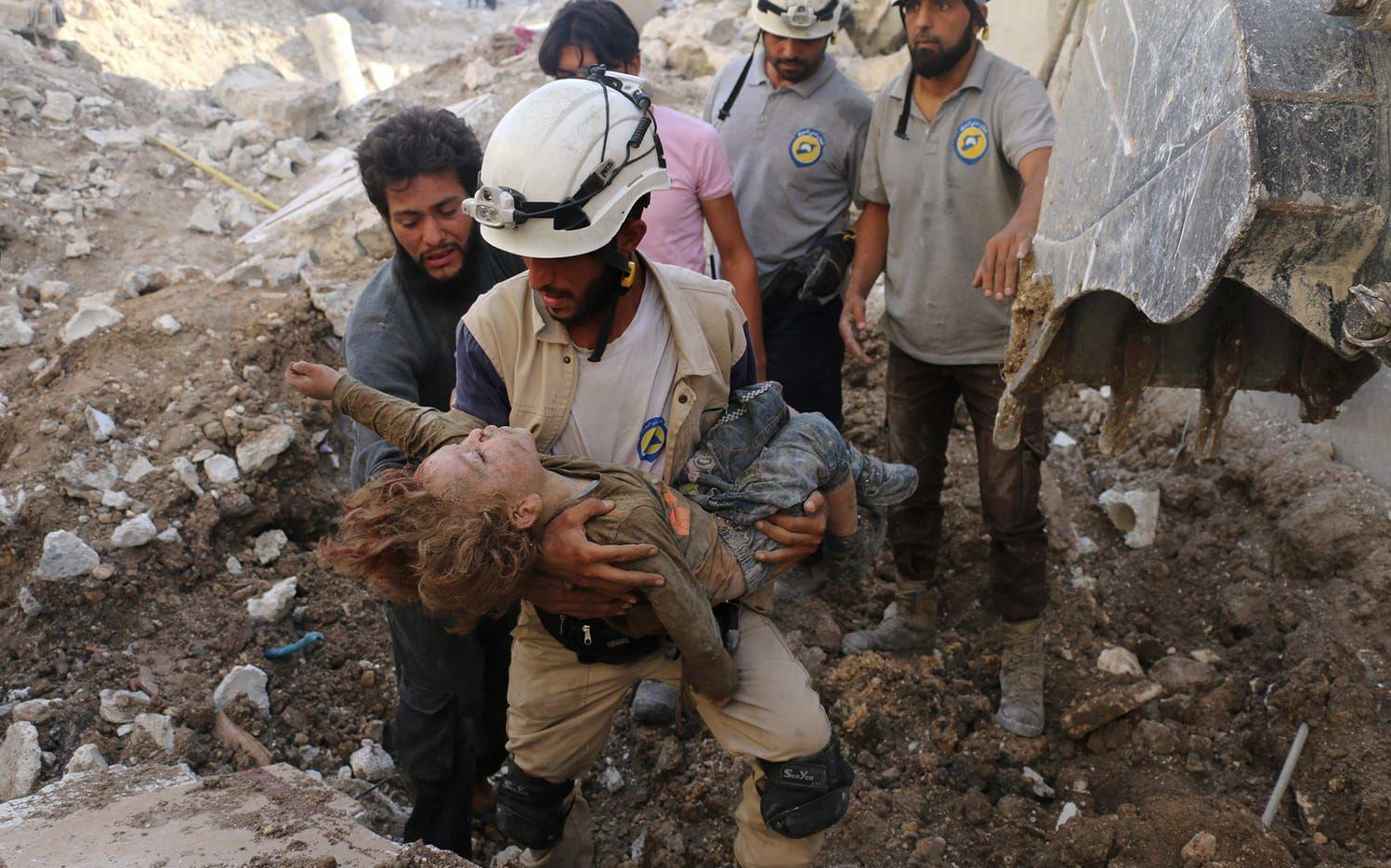 En syrisk hjälparbetare, kända som "De vita hjälmarna", håller i ett barns kropp som grävts fram i rasmassorna efter ännu ett brutalt flyganfall i Aleppo. BILD: Ameer Alhabi