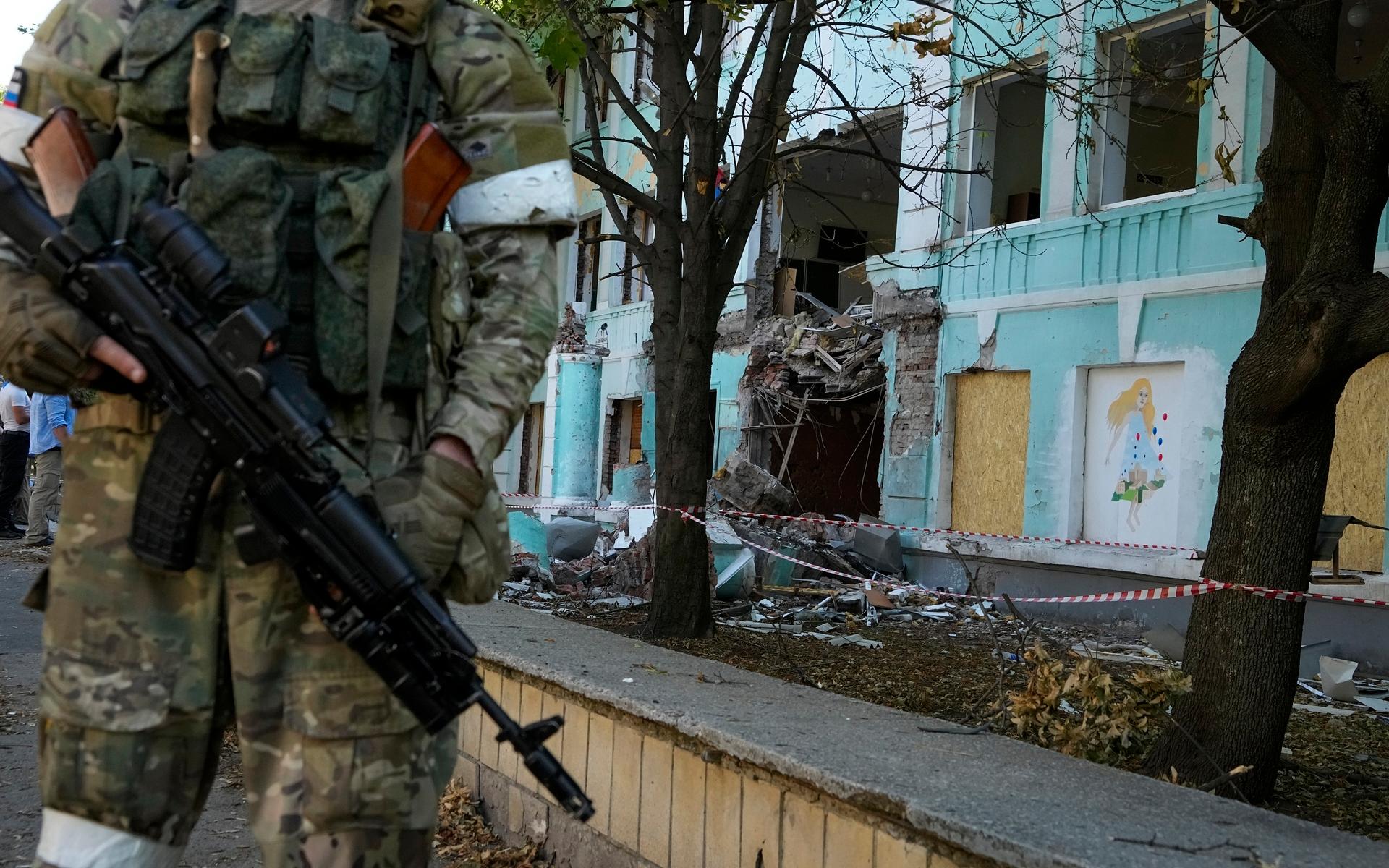En rysk soldat står bredvid en skola som tagit mycket skada i Donetsk. 