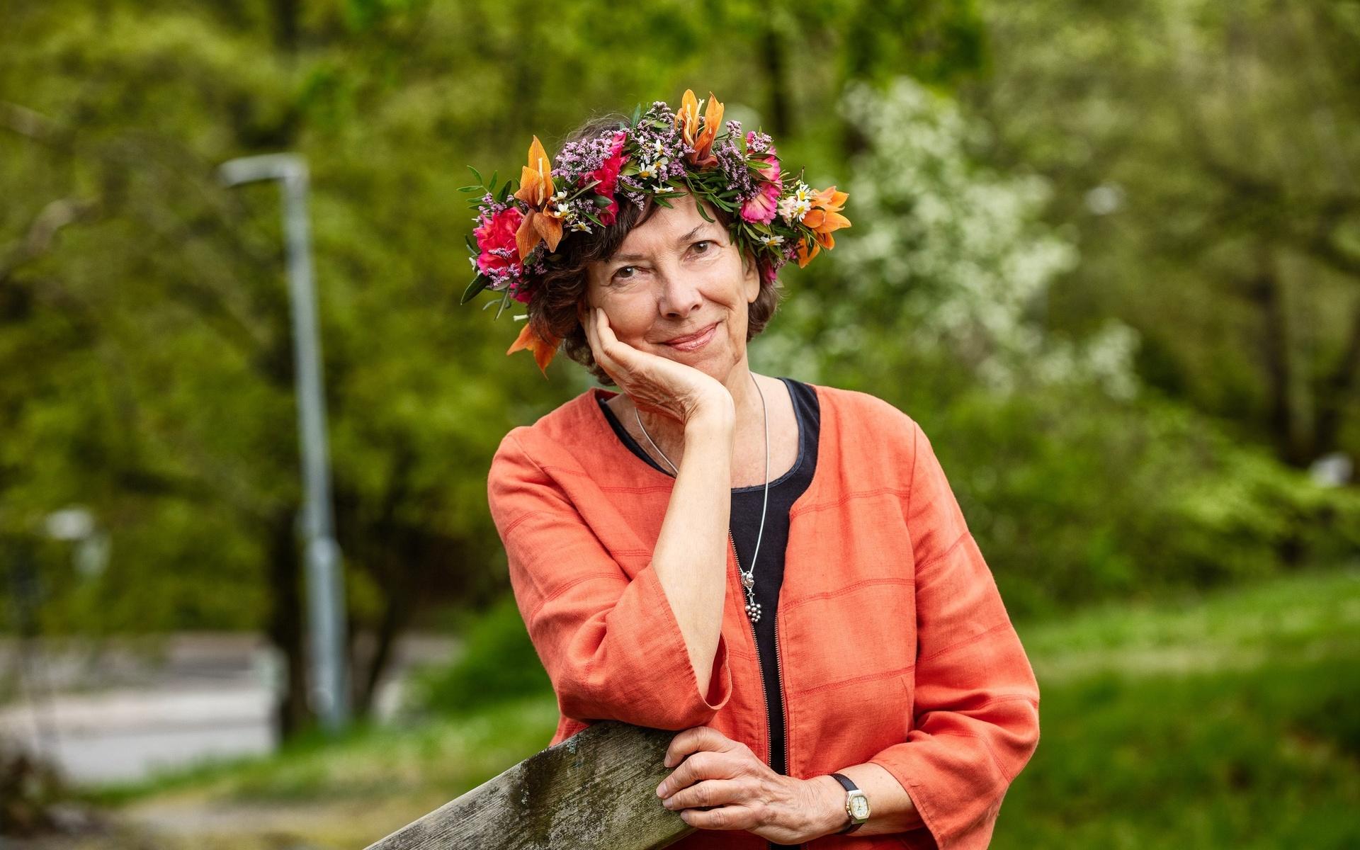 Poeten och essäisten Nina Burton poserar för Sommar i P1. Hon har blomkrans och lutar hakan mot handen. Hon bär en laxrosa kofta över ett svart linne. Det hänger ett silversmycke om hennes hals.