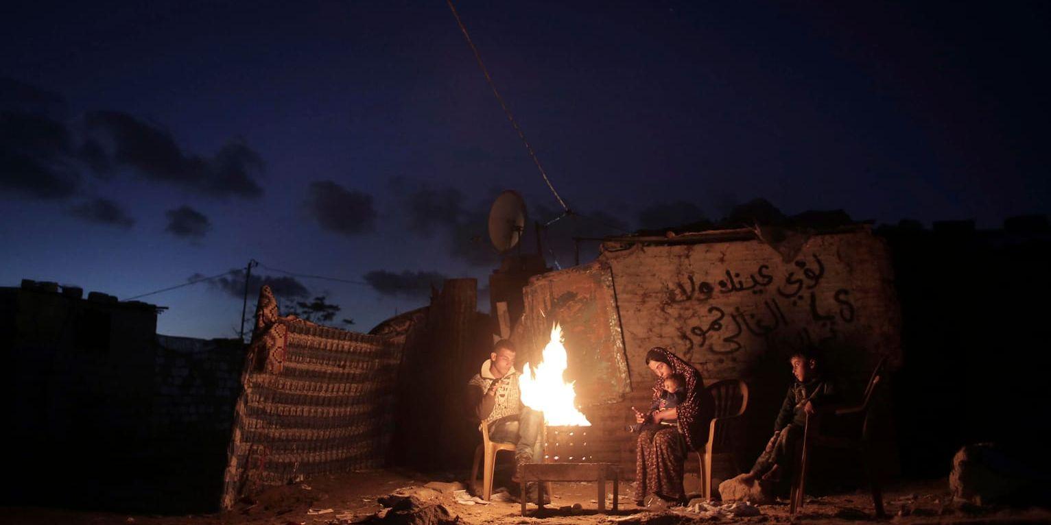 En familj värmer sig vid en öppen eld under ett strömavbrott i södra Gaza. Arkivbild.