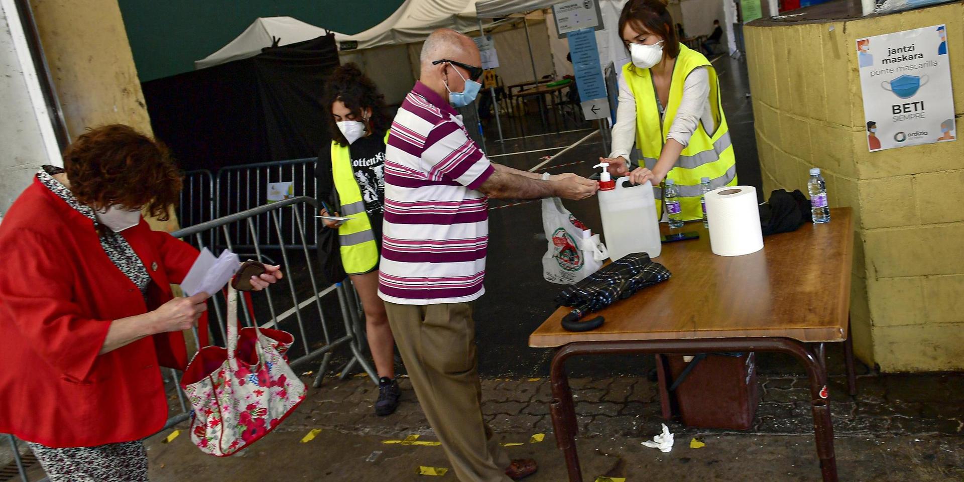 Väljare bär munskydd och använder handsprit i samband med valet. På bilden syns väljare i Baskien.