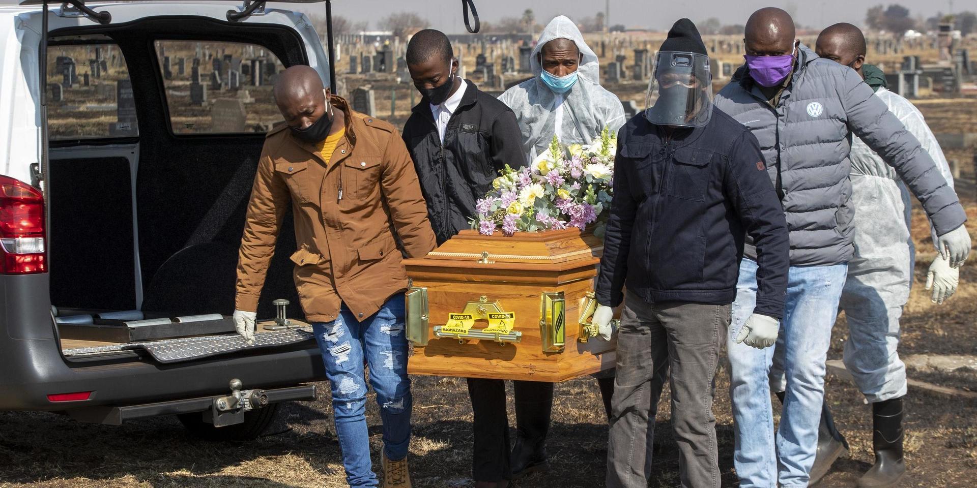 Familjemedlemmar och begravningsarbetare begraver en avliden i covid-19, i Thokoza, öster om Johannesburg, den 23 juli. 