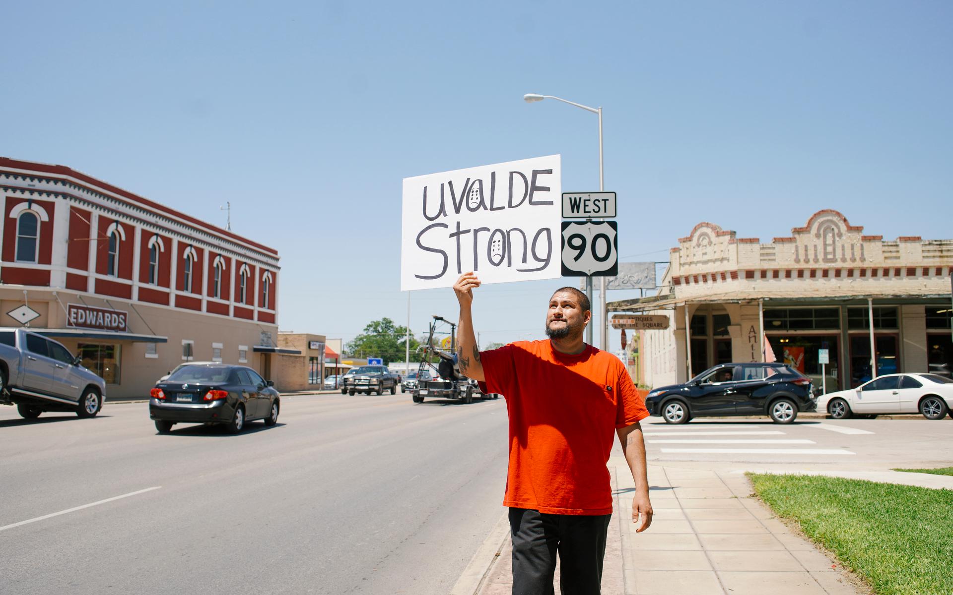Alex Covarrubias holds a sign reading “Uvalde Strong” and walks in front of  a memorial for the children killed in a mass shooting at Robb Elementary school in Uvalde, TX., May 26, 2022. (Photo/Katie McTIernan)