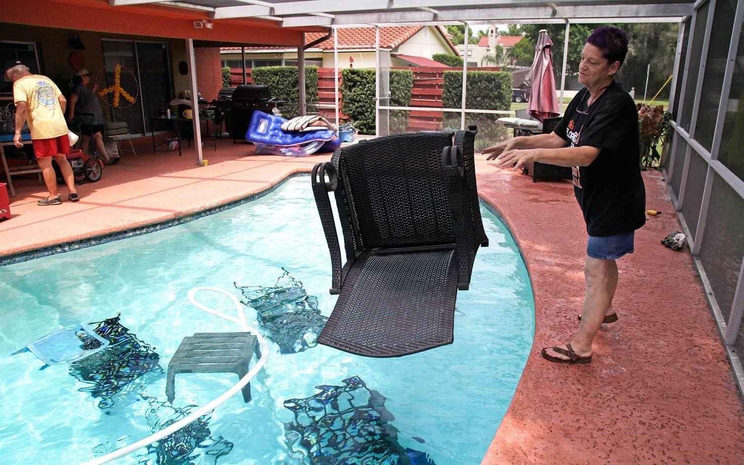 Jackie Kreuter sänker ner sina utemöbler i en pool så att de inte ska flyga iväg när orkanen Irma når land. Bild: TT
