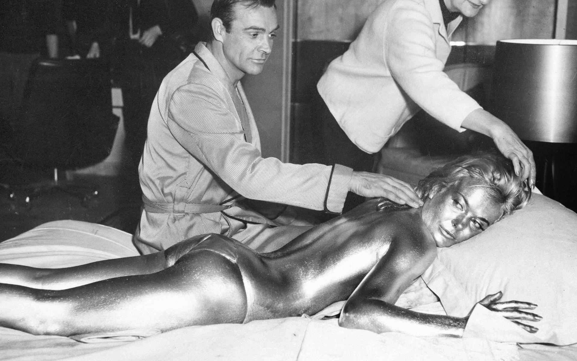 James Bond, spelad av Sean Connery, och Shirley Eaton målad i guld för en scen i Bondfilmen ”Goldfinger”. Filmen var den tredje med Sean Connery i huvudrollen och den första Bondfilmen som regisserades av Guy Hamilton, som skulle komma att regissera ytterligare tre.