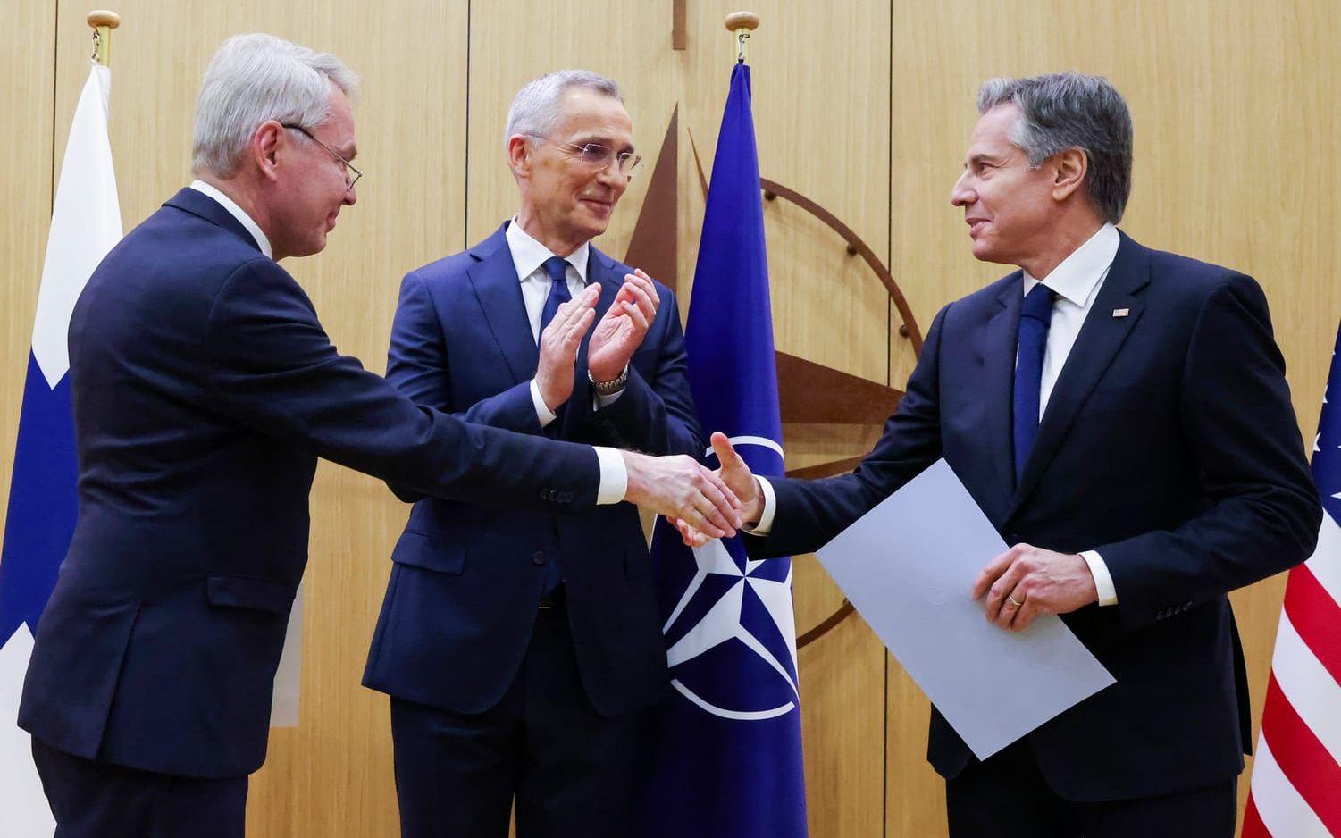 Finlands utrikesminister Pekka Haavisto skakar hand med USA:s utrikesminister Antony Blinken efter att ha överlämnat Finlands anslutningsdokument till Nato. Natos generalsekreterare Jens Stoltenberg applåderar.