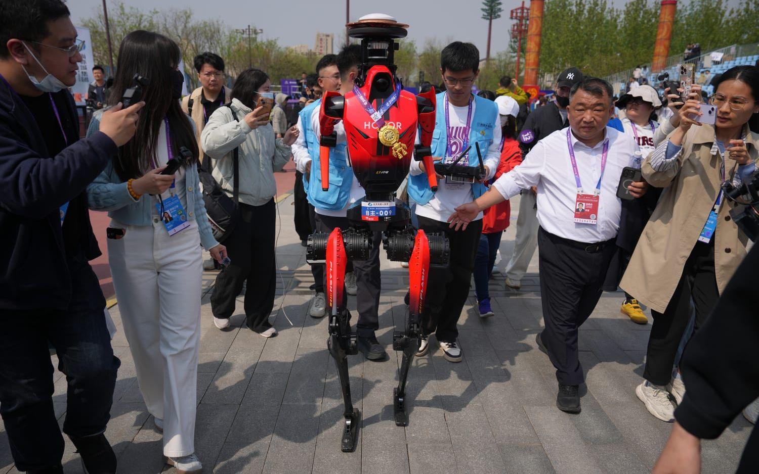 Vinnarroboten från det kinesiska företaget Honor jagas av journalister efter halvmaratontävlingen för humanoida robotar i Peking, Kina på söndagen. 