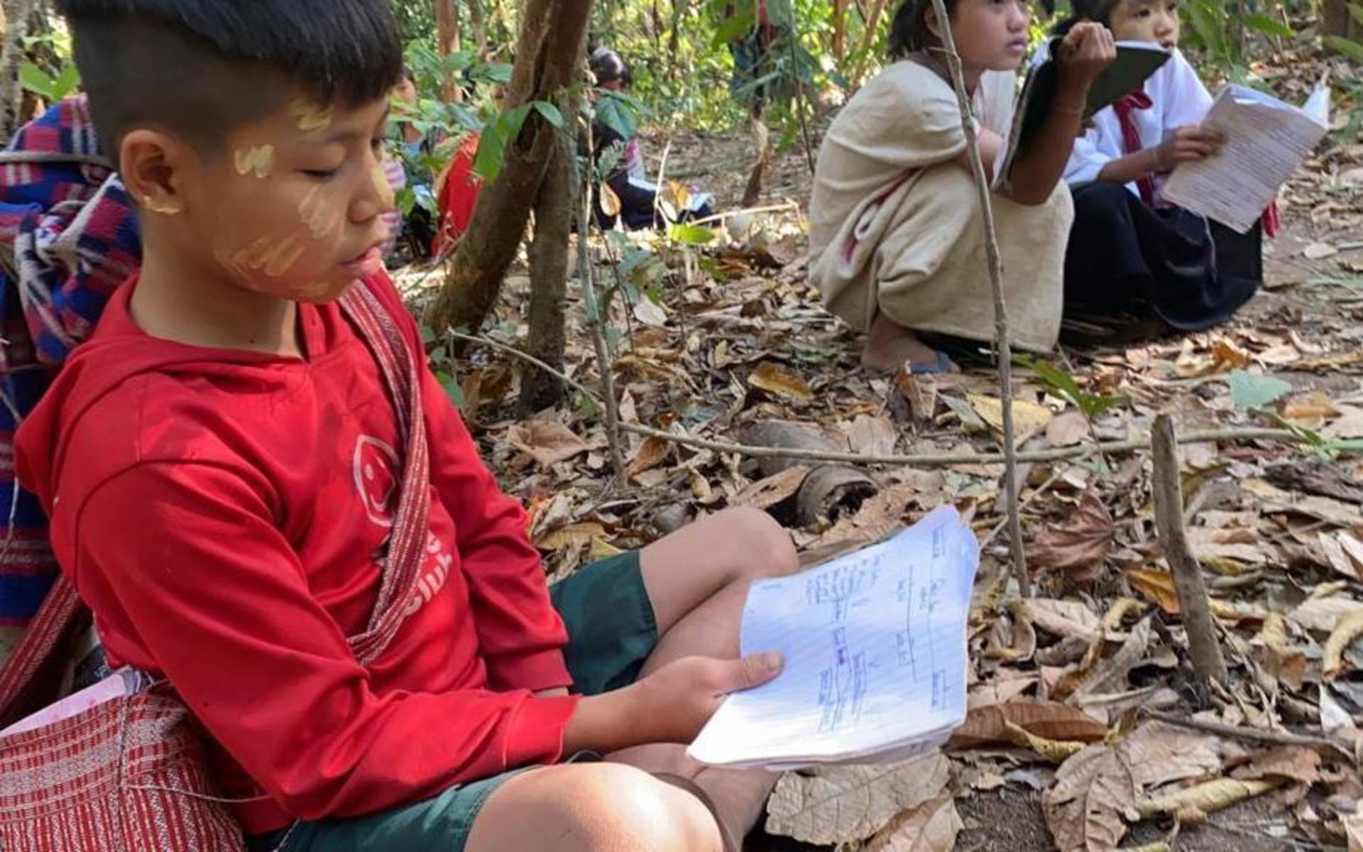 Barn läser läxor och gör skolarbete i djungeln i norra Karenstaten. De flydde tillsammans med sina familjer efter att Myanmars militär besköt deras by med granater. 