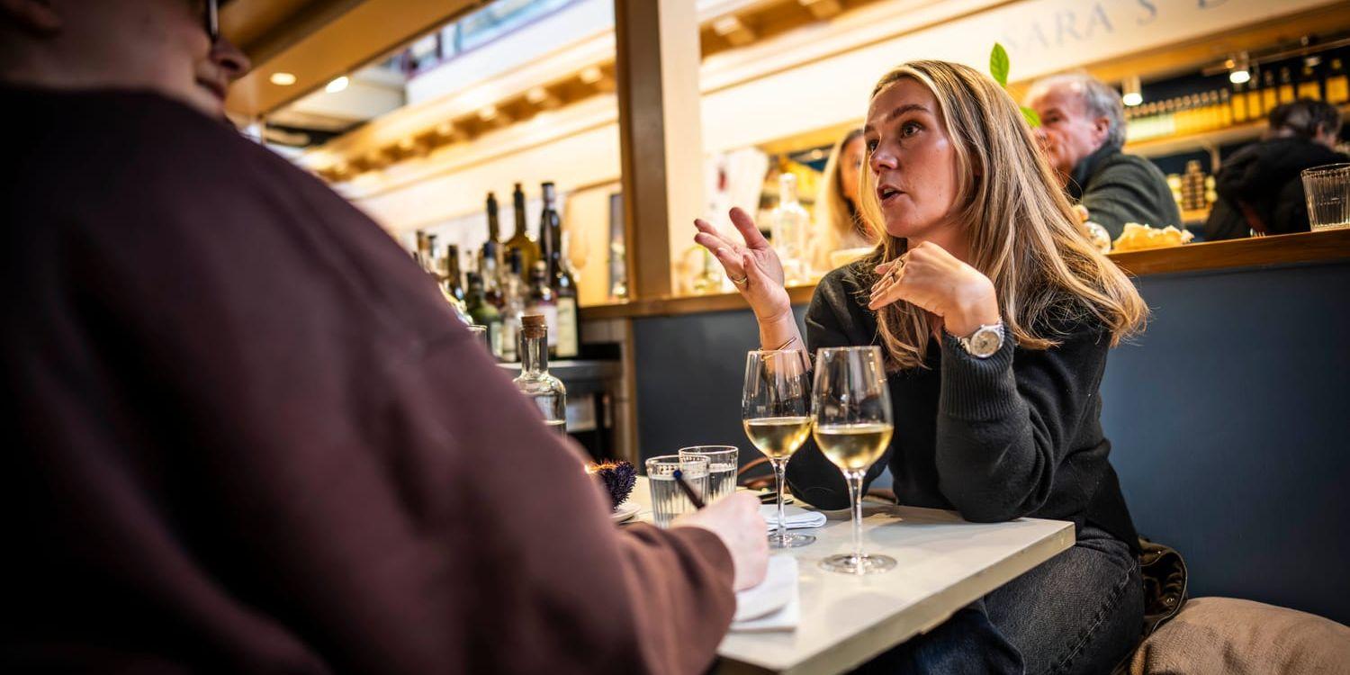 Johanna Bradford sitter vid ett litet bord med två glas vin på inne i Saluhallen.