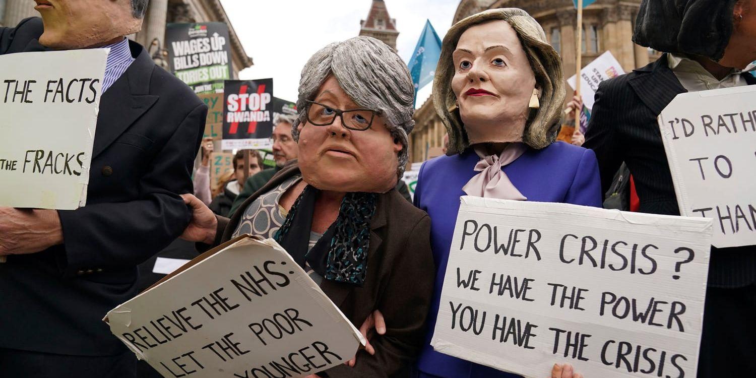 Demonstranter med masker i papier-maché föreställande den brittiska premiärministern Liz Truss till höger, och biträdande premiärminister Therese Coffey till vänster protesterar mot regerings politik utanför regeringspartiet Tories kongress i Birmingham