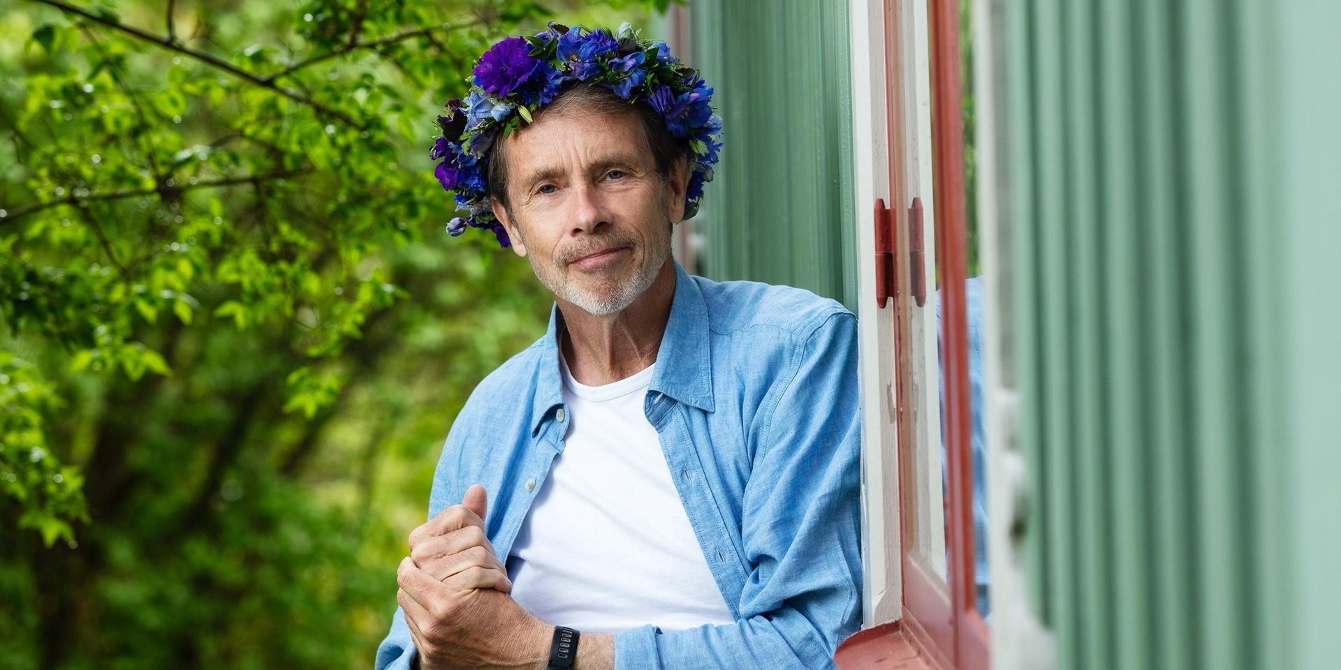 Jacob Hård (af Segerstad) poserar inför Sommar i P1, han har vit t-shirt, svarta byxor. Skärp med metallspänne, blå skjorta och en blomsterkrans med blåa blommor.