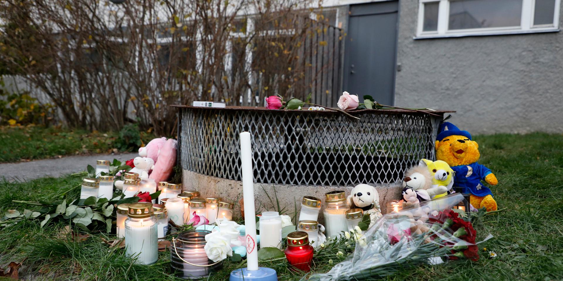 Gosedjur, blommor och ljus har lagts ner vid den plats där två barn hittades med livshotande skador utanför ett bostadshus i Hässelby i söndags kväll. Ett av barnen avled senare av sina skador. Tillståndet för det andra barnet är fortfarande allvarligt.