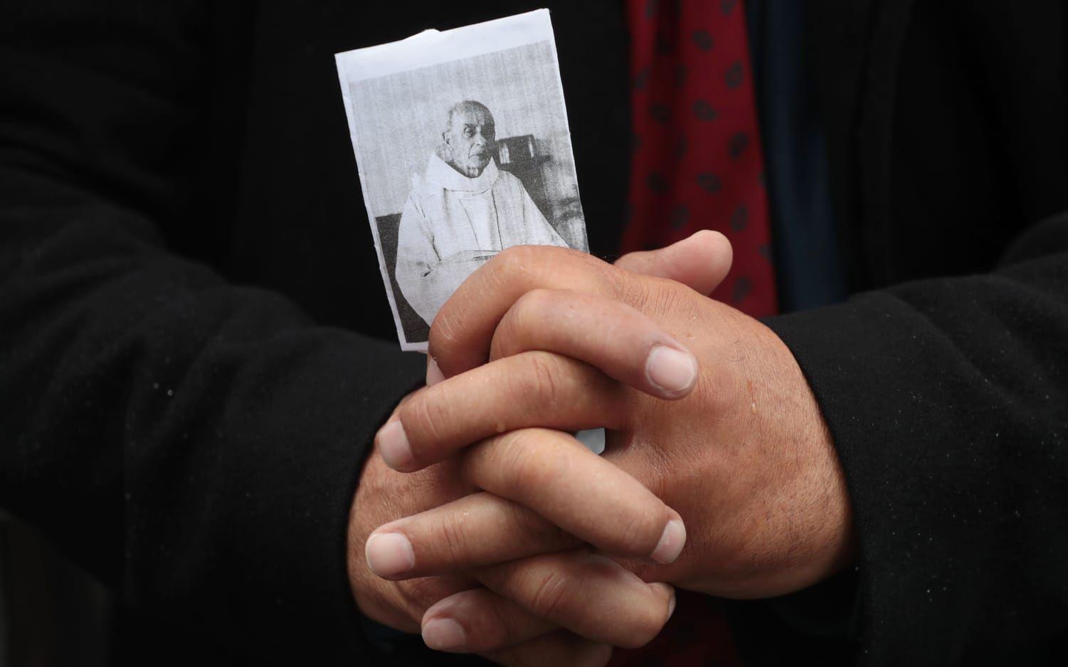 En åskådare höll upp en bild på Jacques Hamel och knöt sina händer i bön utanför katedralen. Bild: TT