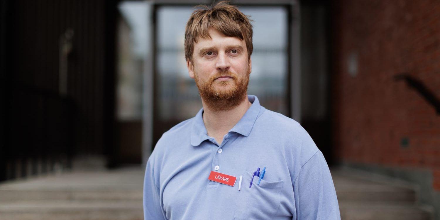 En man i blå tröja och en skylt på bröstet där det står läkare. 
