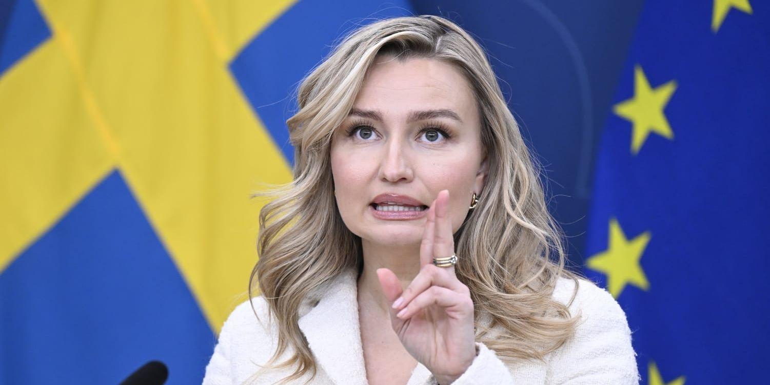 Ebba Busch (KD) i vit kavaj mot en bakgrund av svenska och EU:s flaggor. 