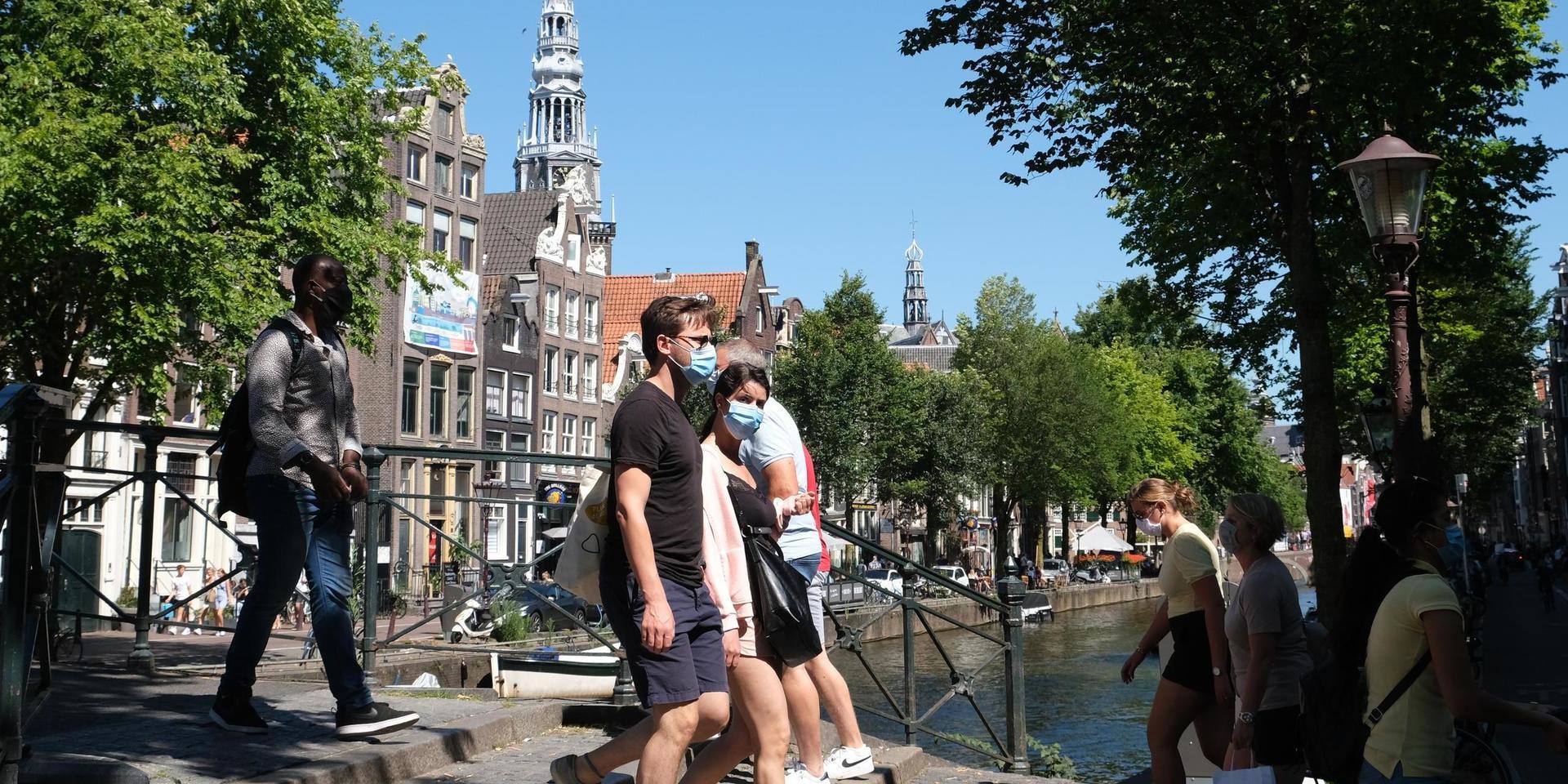 Människor promenerar över en bro i Nederländernas huvudstad Amsterdam, där krav på munskydd nyligen införts på vissa platser.