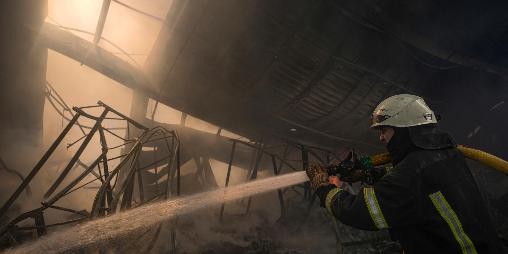En ukrainsk brandman släcker en eld i ett förstört varuhus i Kievs utkant. Striden har hårdnat utanför huvudstaden.