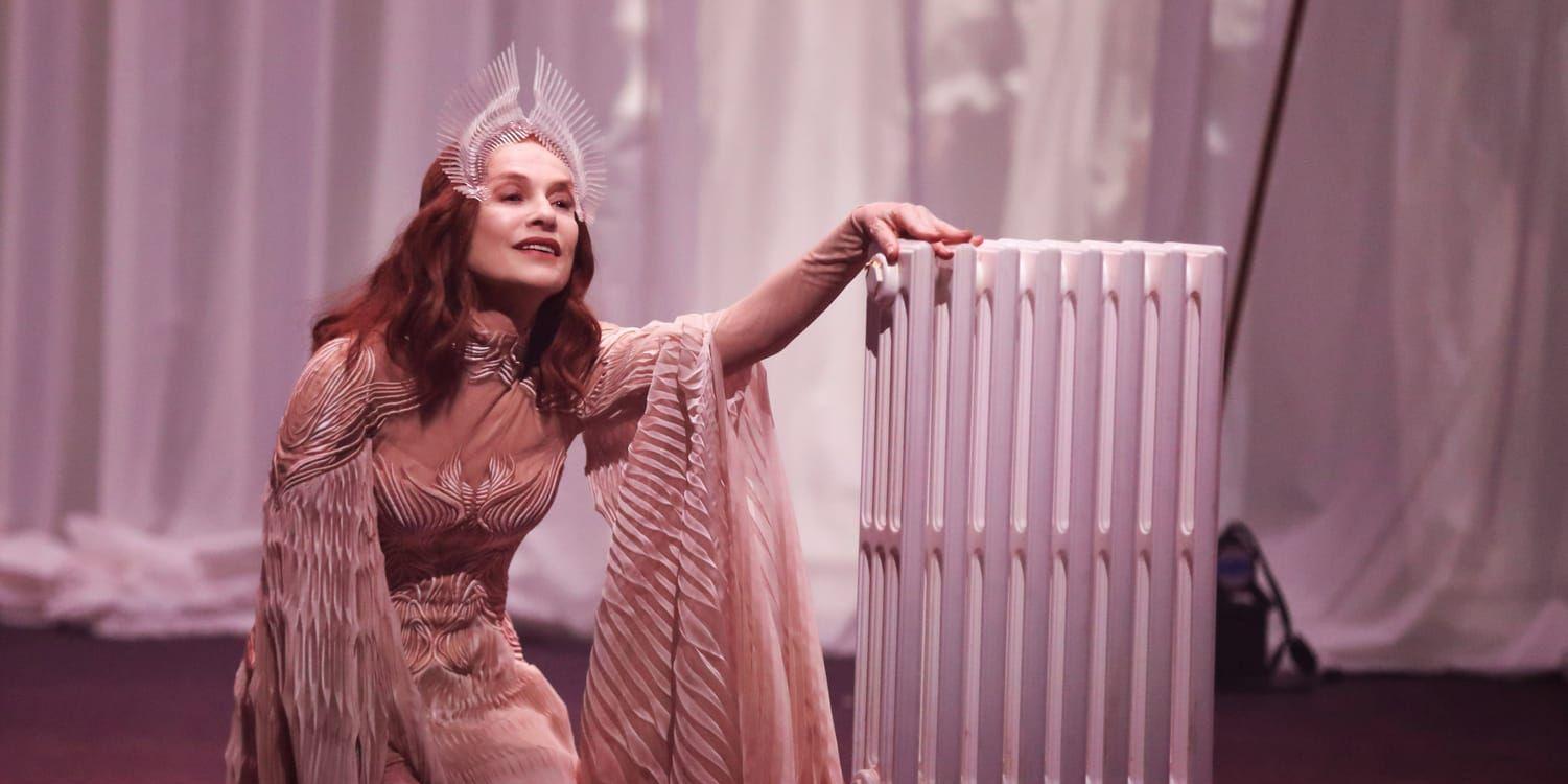 Isabelle Huppert som rollfiguren Bérénice, i lång svepande klänning och hög tiara, på en teaterscen.