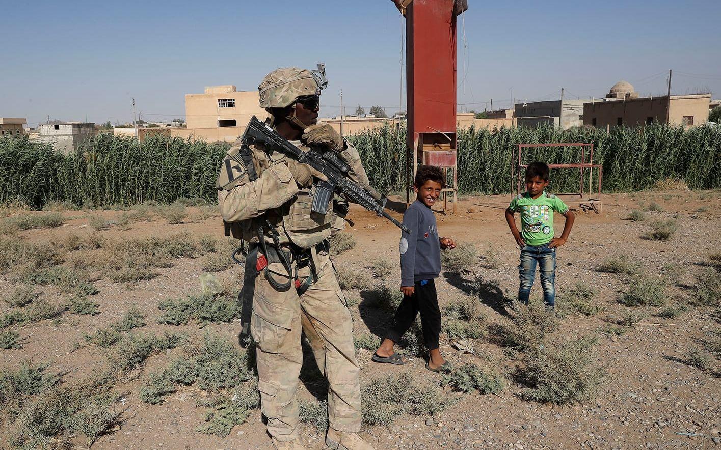 En amerikansk soldat och några syriska barn står vid en väg nära al-Raqqa. USA har upp till 1000 militärer i Syrien, huvudsakligen där för att träna och utbilda trupper till att slåss mot IS.FOTO: Hussein Malla/AP
