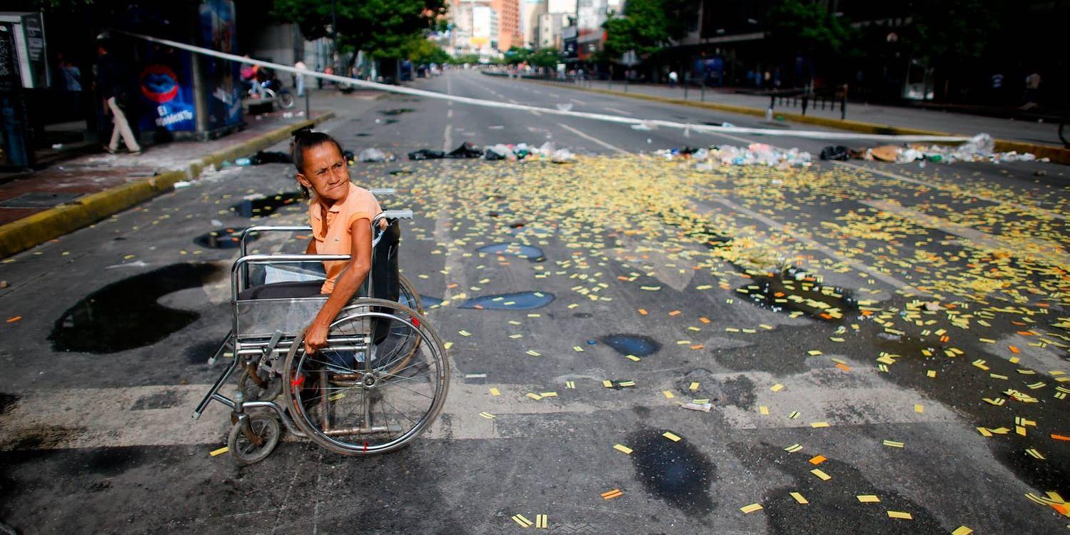 En rullstolsburen kvinna passerar en vägspärr som satts upp av regeringskritiker vid en gata i Caracas på torsdagsmorgonen.