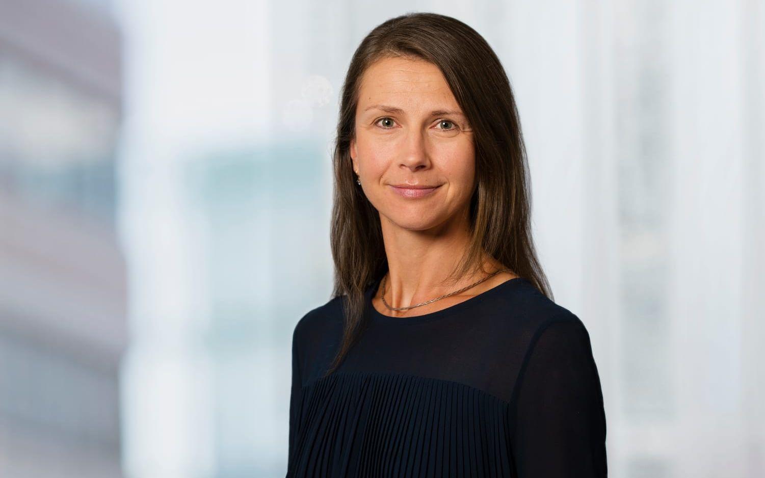 Kvinna med brunt hår, svart tröja i fokus, suddig bakgrund.