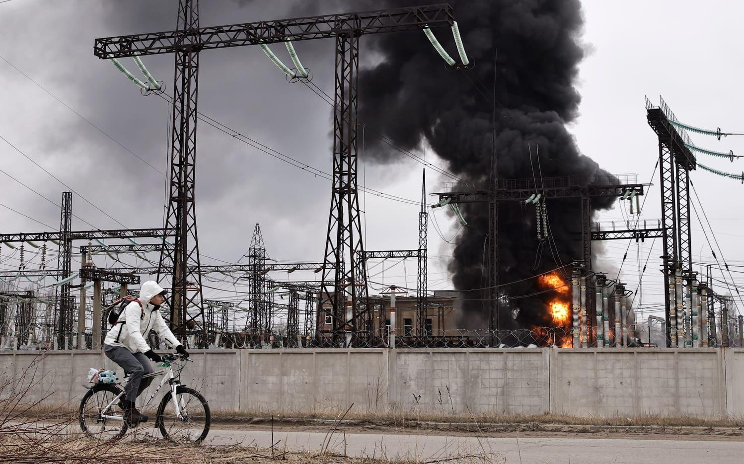 En man cyklar förbi en brinnande elcentral i Charkiv som attackerats av Ryssland i mars i år.