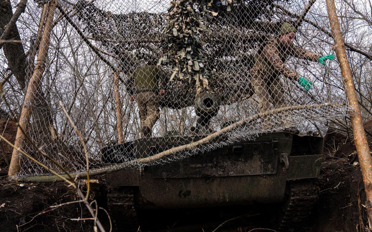 Ukrainska soldater täcker en artilleripjäs för att den ska bli svårare att upptäcka för Rysslands så kallade kamikazedrönare. Bilden togs vid fronten i Bachmut i fredags.