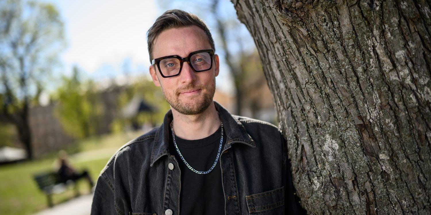 Axel Pileby i svart jeansjacka och lutar sig mot ett träd i en parkmiljö.