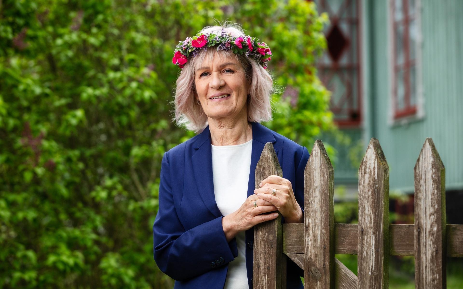 Gunhild ”Ninis” Rosqvist poserar för Sommar i P1. Hon har blå kavaj och vit topp. Hon har blomsterkrans och kort frisyr. 