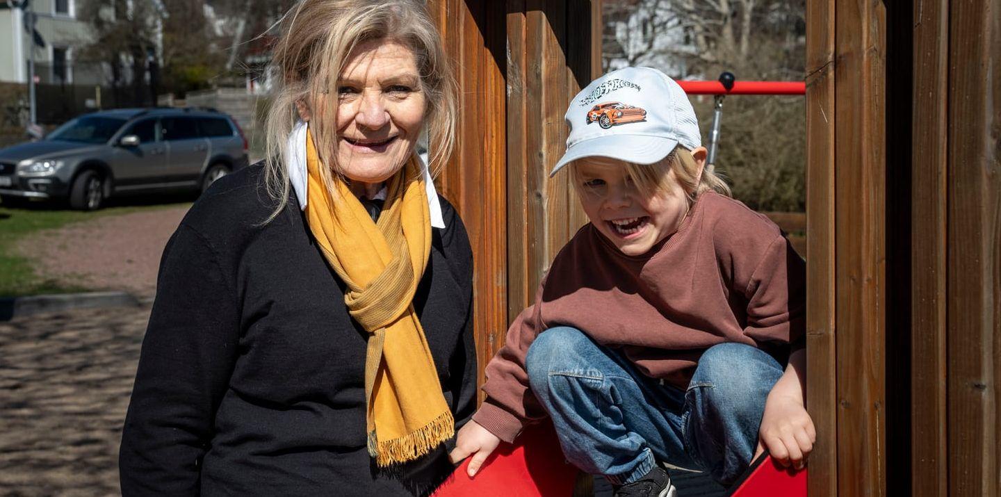 Kvinna står intill rutschkana där pojke med keps tar sats för att åka.