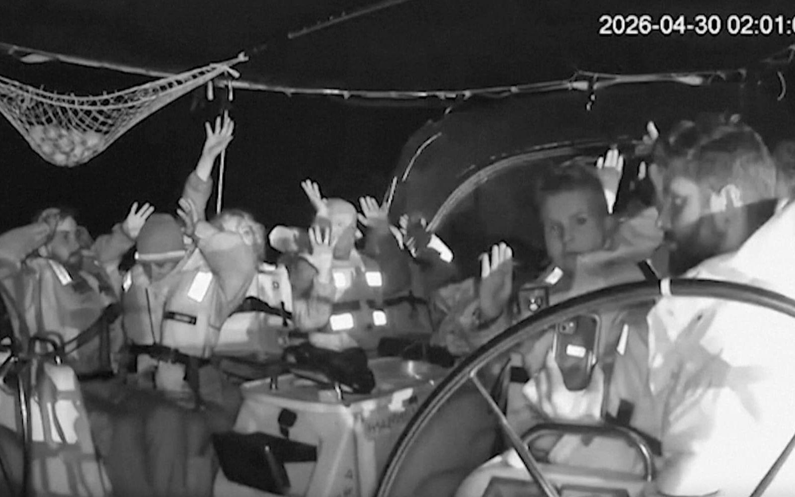 Aktivister ombord på en av konvojens båtar sträcker upp händerna i luften i samband med att Israel stoppar fartyget tidigt på torsdagen. Stillbild från en övervakningskamera.