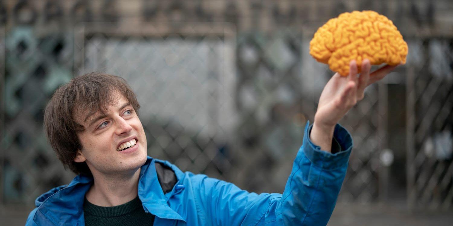 En man i blå jacka håller upp en modell av en hjärna.