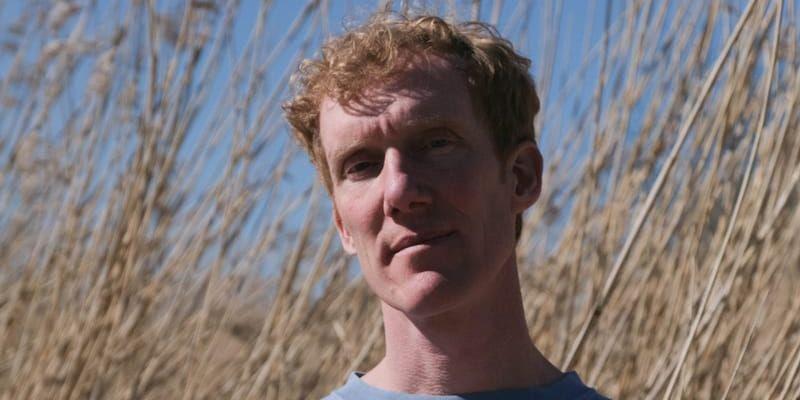 Kapten Röd i blå tröja står framför hög vass. 