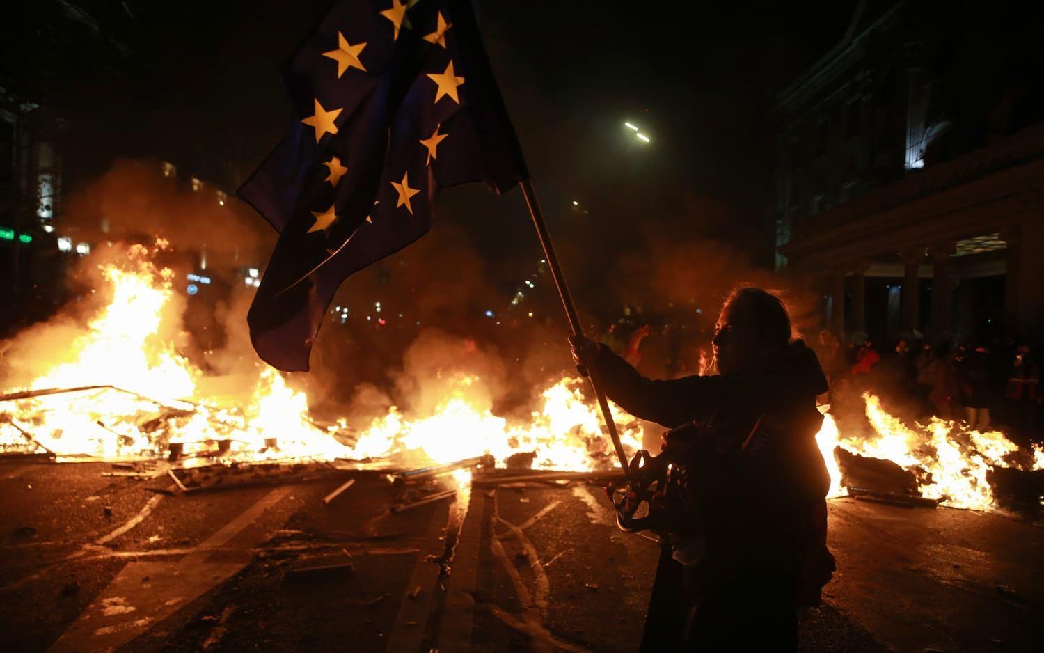 En demonstrant med en EU-flagga framför en brinnande barrikad i Georgiens huvudstad Tbilisi natten mot tisdagen.