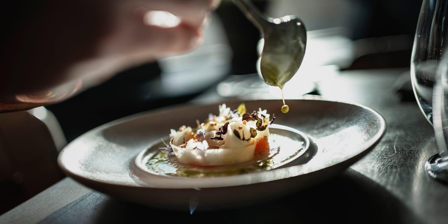 Sås droppas från en sked på en tallrik med vackert upplagd mat.