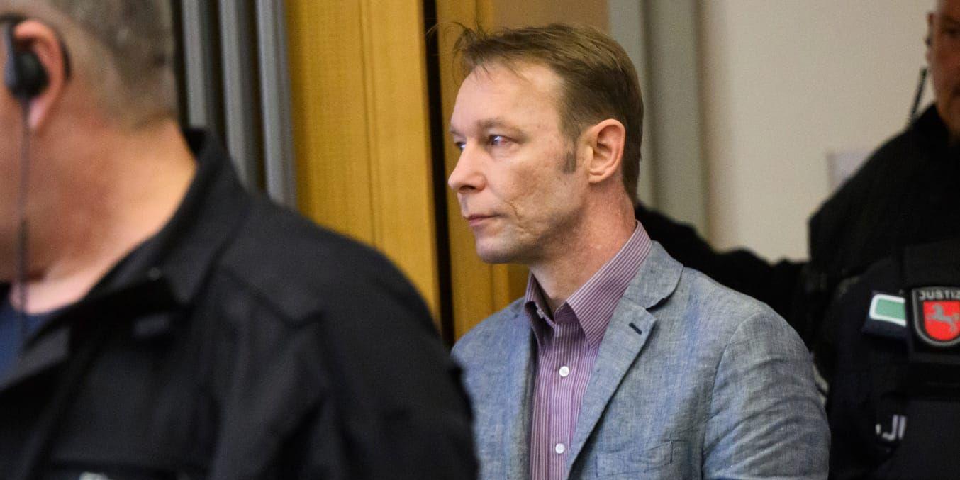 Man i grå kostym och skjorta förs in i rättssal av två vakter.