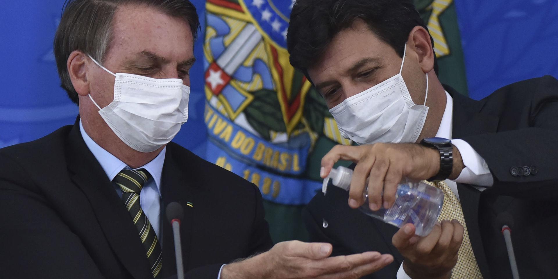 Brasiliens hälsominister Luiz Henrique Mandetta, till höger, trycker ut handsprit i sin chefs, president Jair Bolsonaros, händer under en presskonferens vid presidentpalatset i Brasilia den 18 mars. 
