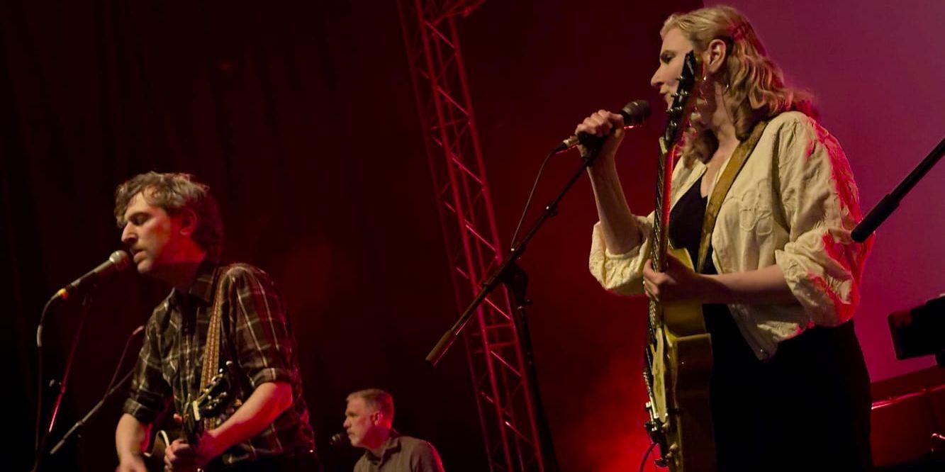 Great Lake Swimmers tre medlemmar står och sitter på rad och sjunger i mikrofoner på en scen.