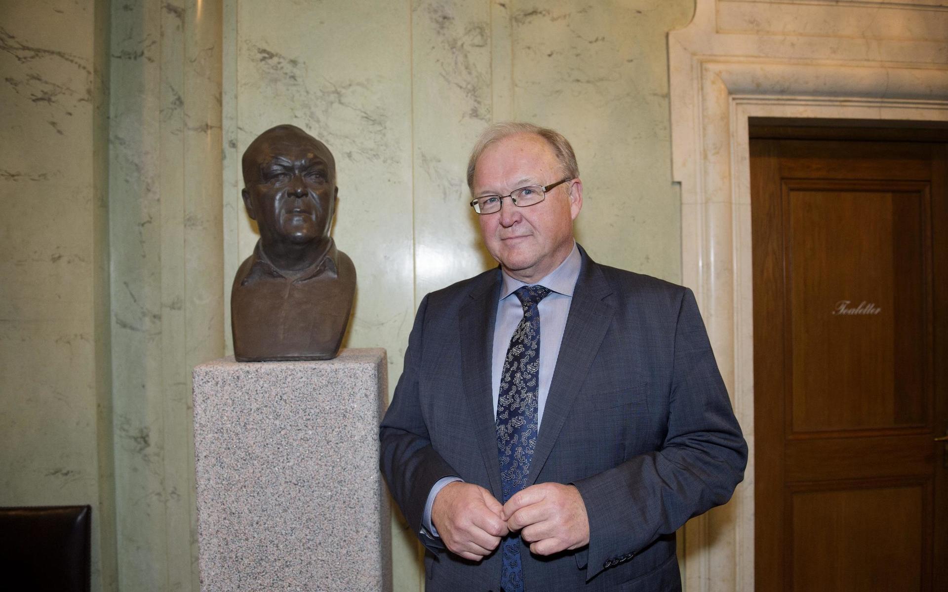 Förre statsministern Göran Persson poserar vid porträttbysten av honom i Riksdagshuset.