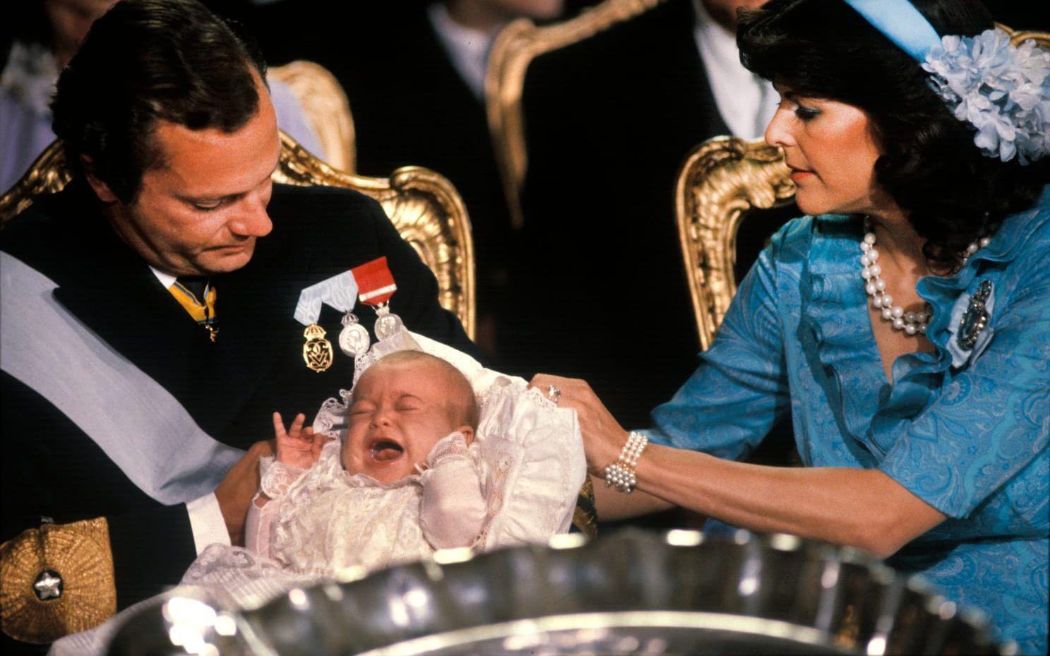 1982: Prinsessan Madeleine gråter i sin far kung Carl XVI Gustafs famn under sitt dop i Slottskyrkan 31 augusti.
