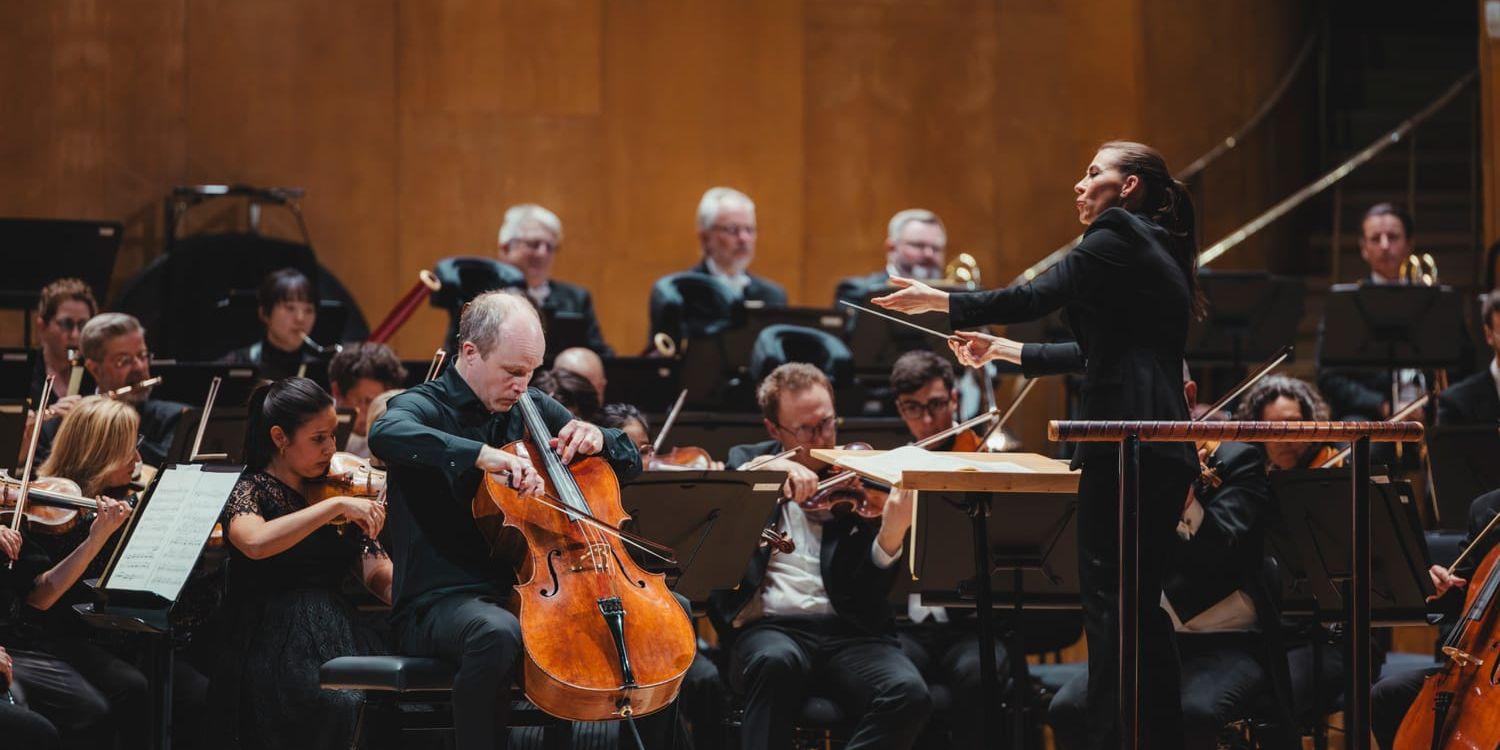 Cellisten Claes Gunnarsson sittande till vänster omgiven av Göteborgs Symfoniker och med dirigent Marta Bartolinska med höjda armar till höger. 