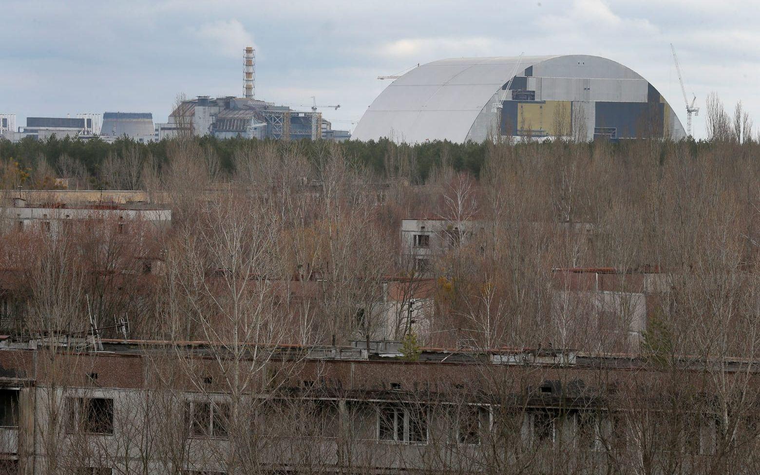 I förgrunden den övergivna staden Prypyat. I bakgrunden syns Tjernobyl och den nya konstruktionen som ska täcka över reaktor 4.