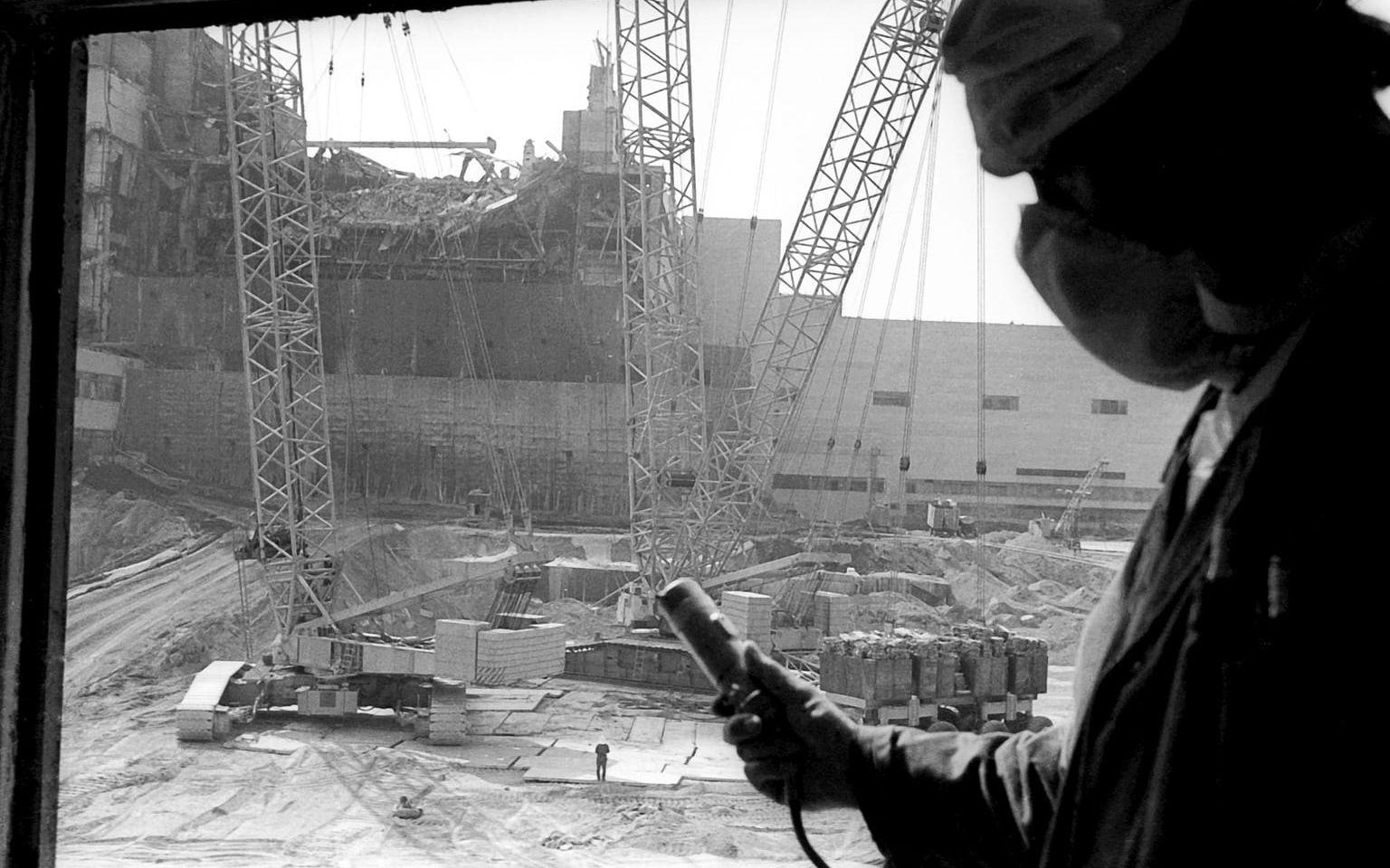 En man med dosimeter mäter strålningen under arbetet med att täcka över reaktor fyra. I bakgrunden syns sarkofagen i cement som täcker olycksplatsen.